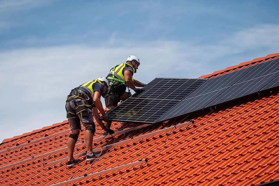 Dva montážníci instalují fotovoltaický panel na střechu firemní budovy